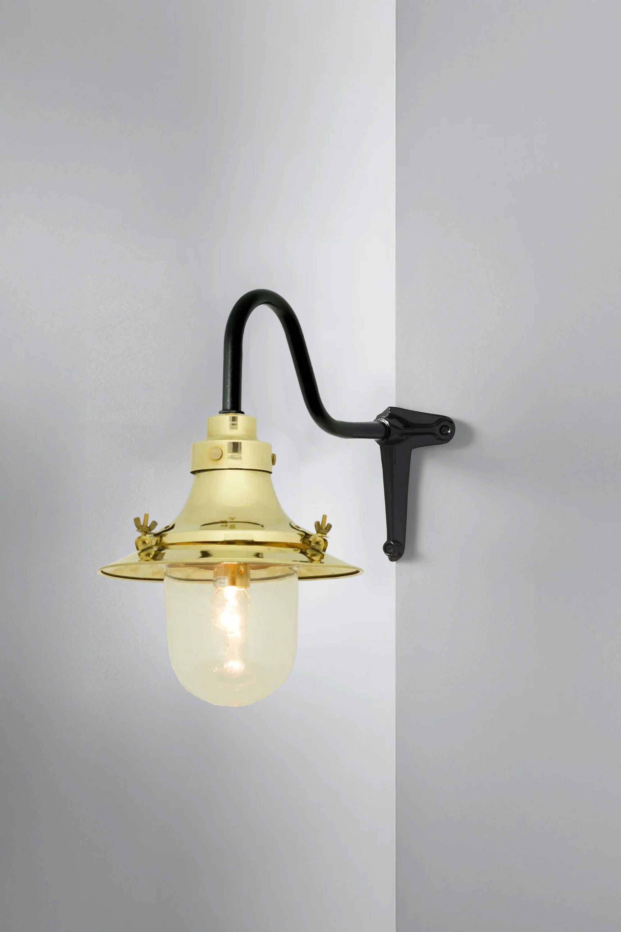 Wall-mounted light fixture with brass finish and glass shade on a gray background