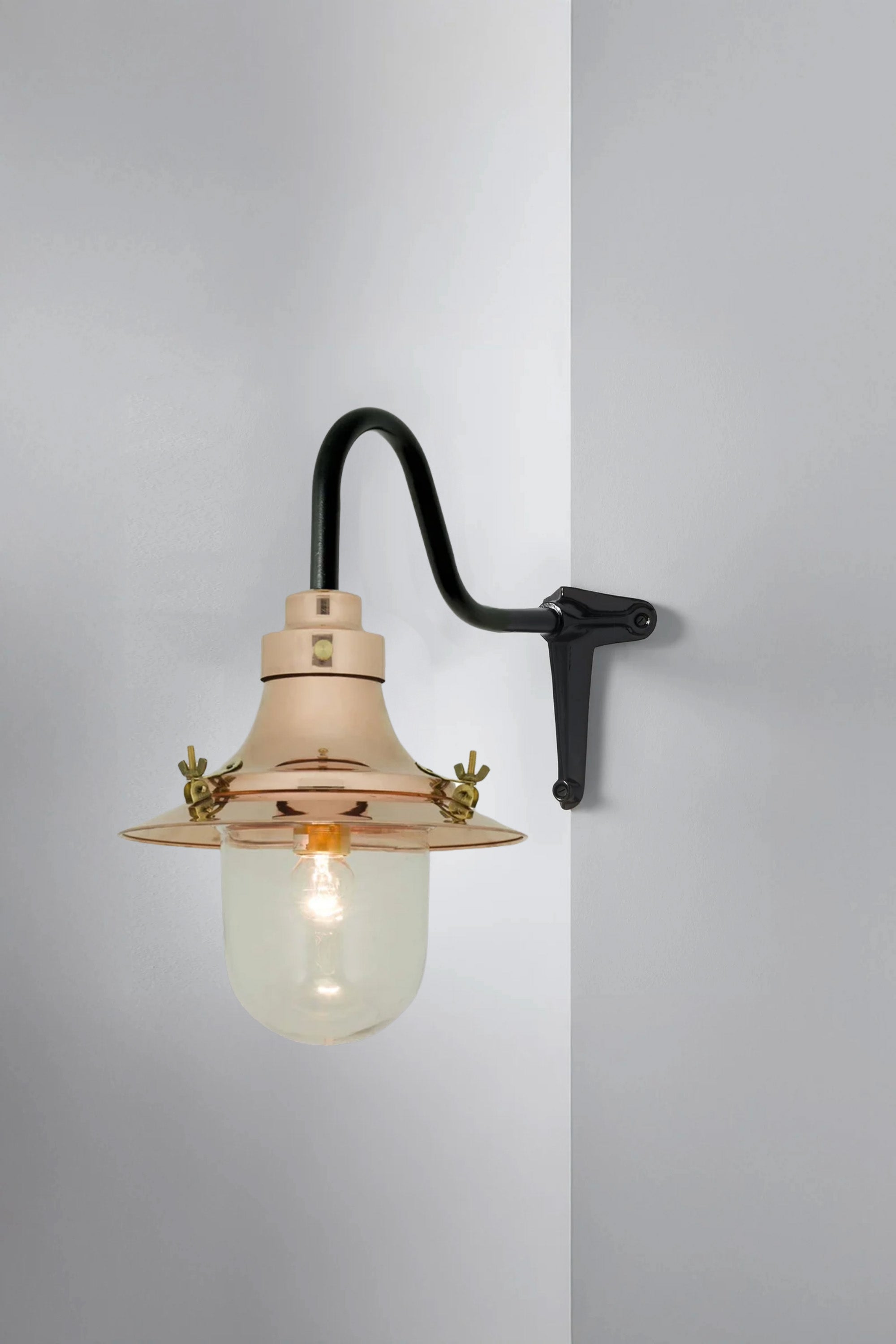 Wall-mounted light fixture with glass shade and brass accents on a gray background