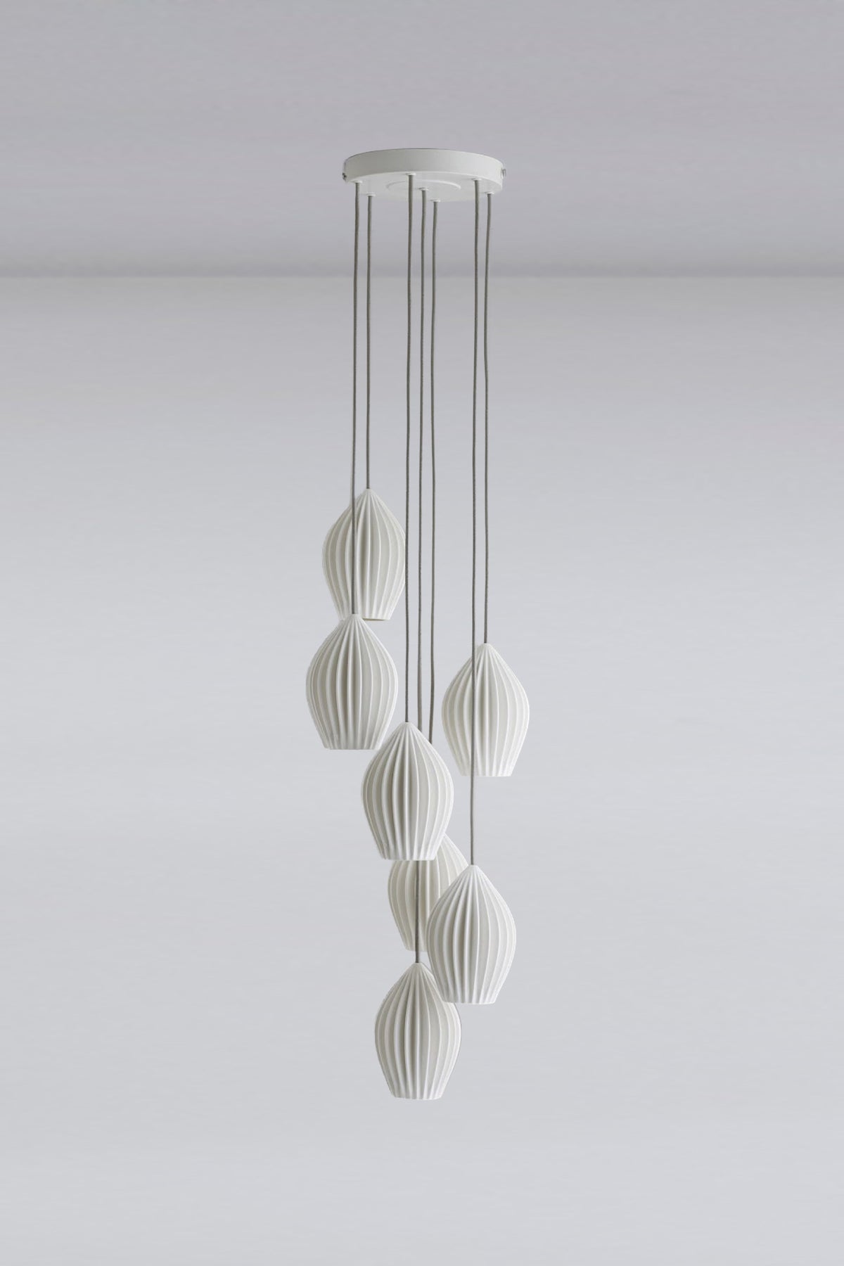 A ceiling-mounted pendant light fixture with a grouping of seven white elements in an indoor setting.