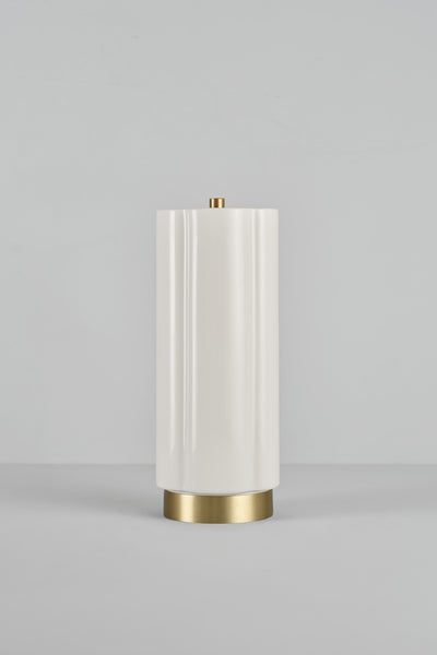 A modern table lamp with a tall, cylindrical off-white shade featuring subtle vertical fluting, supported by a brushed gold metal base and topped with a small gold finial, set against a neutral gray studio background.