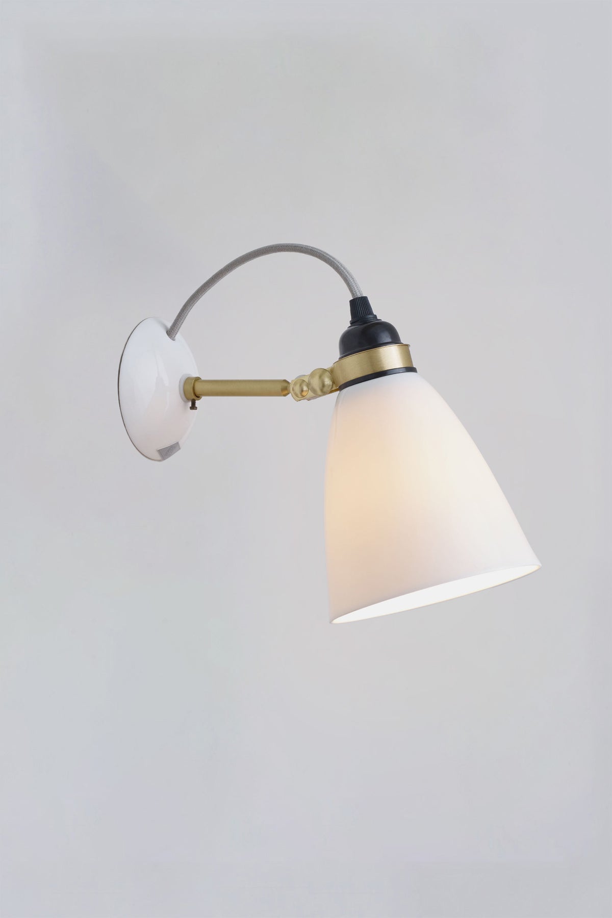 Hector 30 wall light with a white bone china shade and grey cable, illuminated.