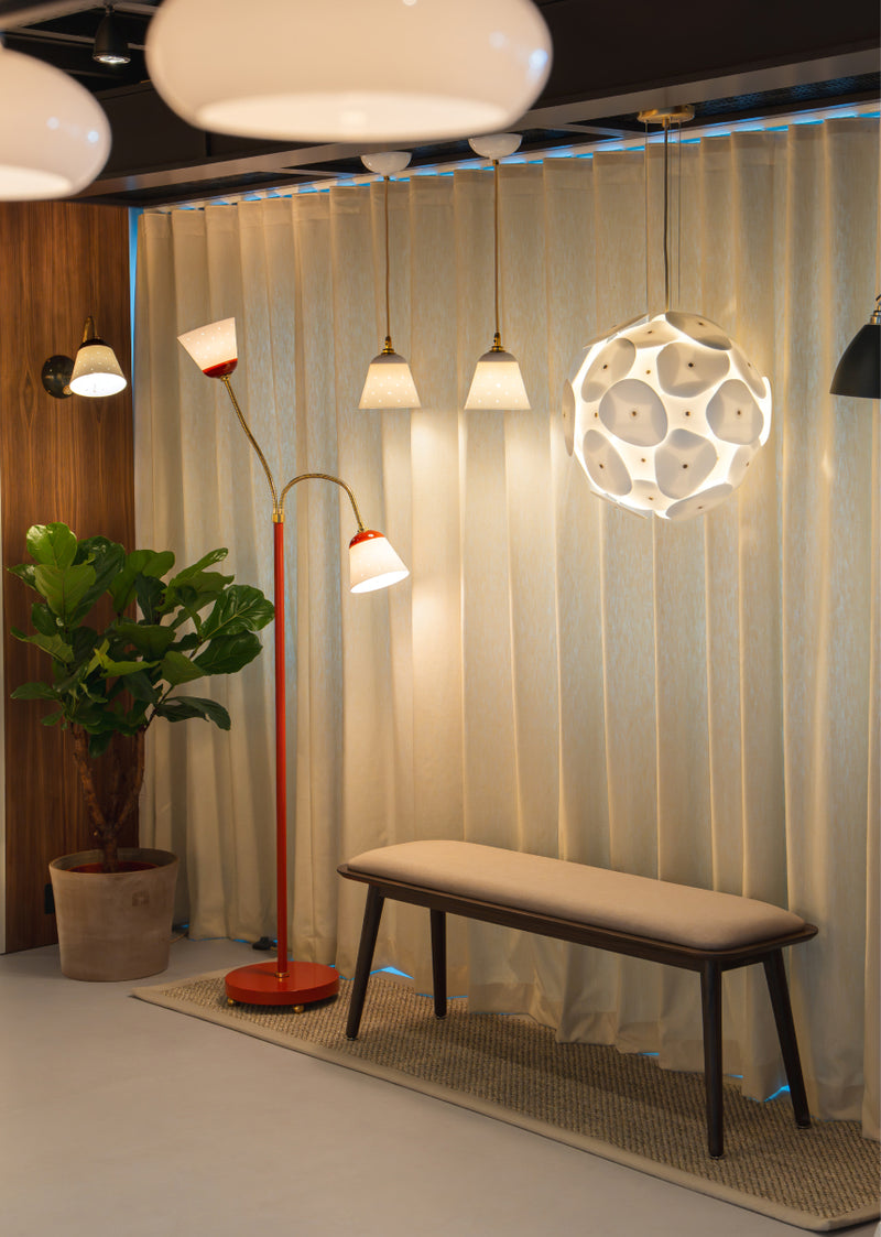 Interior room with decoractive pendant lights, a floor light and a wall light in front of fabric curtains, paired with a upholstered wooden bench.