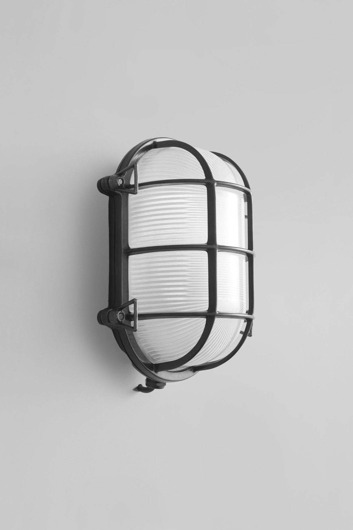 A wall-mounted brass bulkhead light with a protective cage around the bulb.