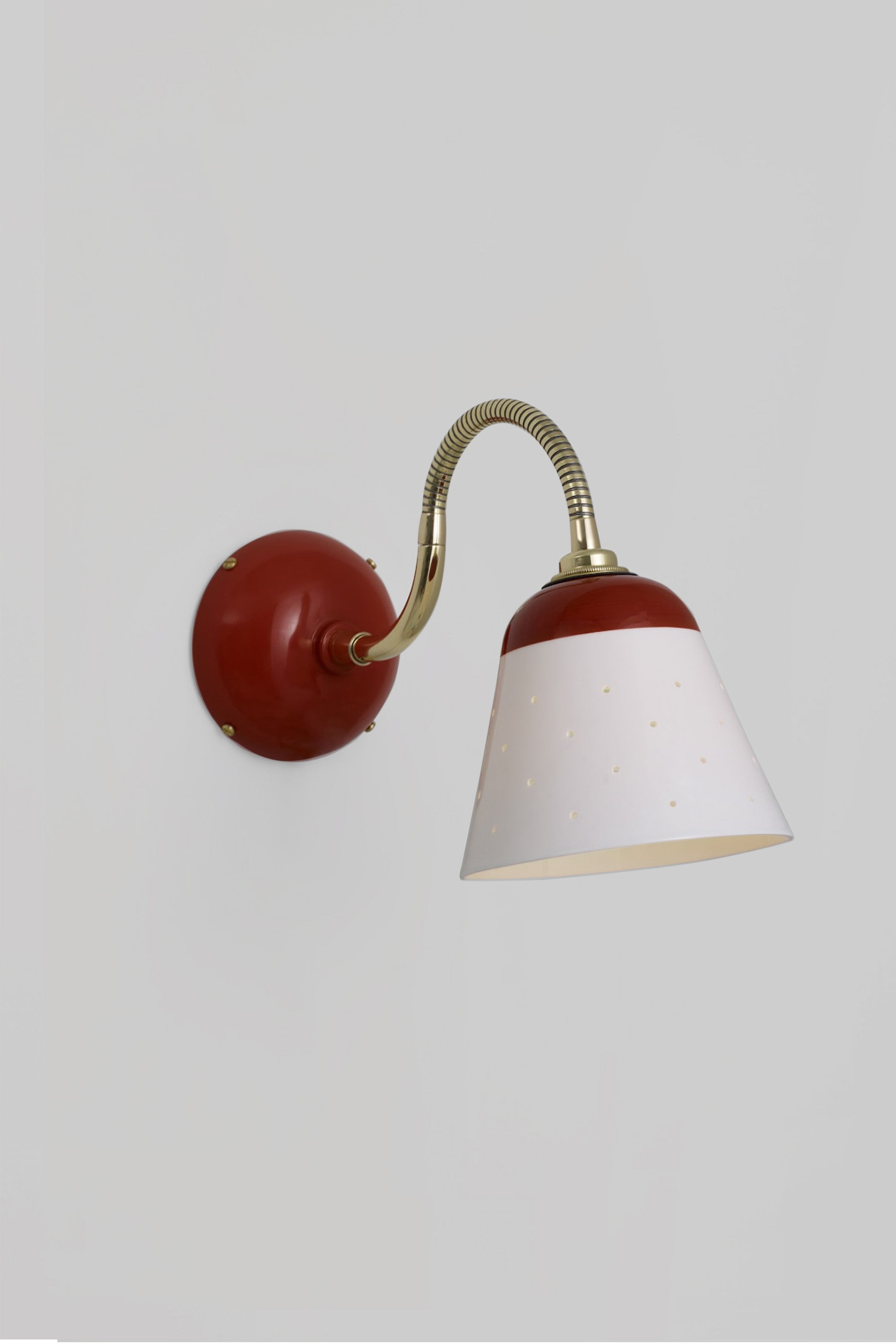 A wall-mounted light fixture with a white shade, gold-colored metal arm, and red wall mount.