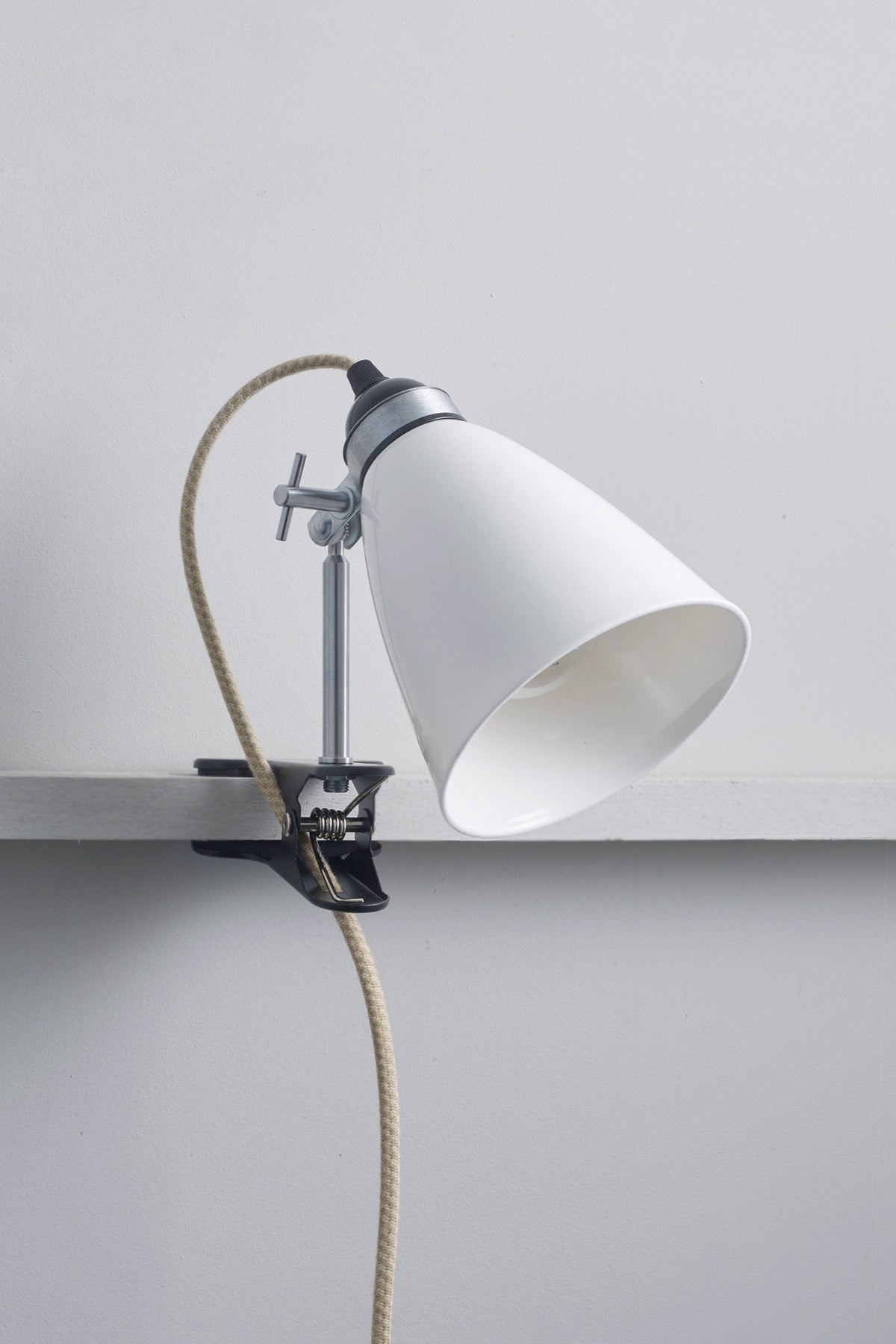 White lamp with a clip and coiled cord on a light gray background