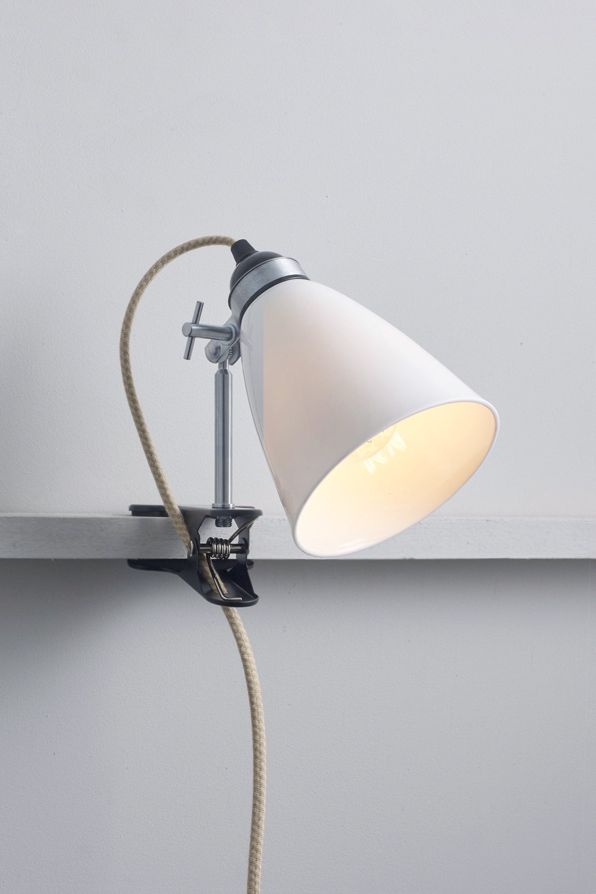 Clip-on wall lamp with white shade and visible bulb on a gray background