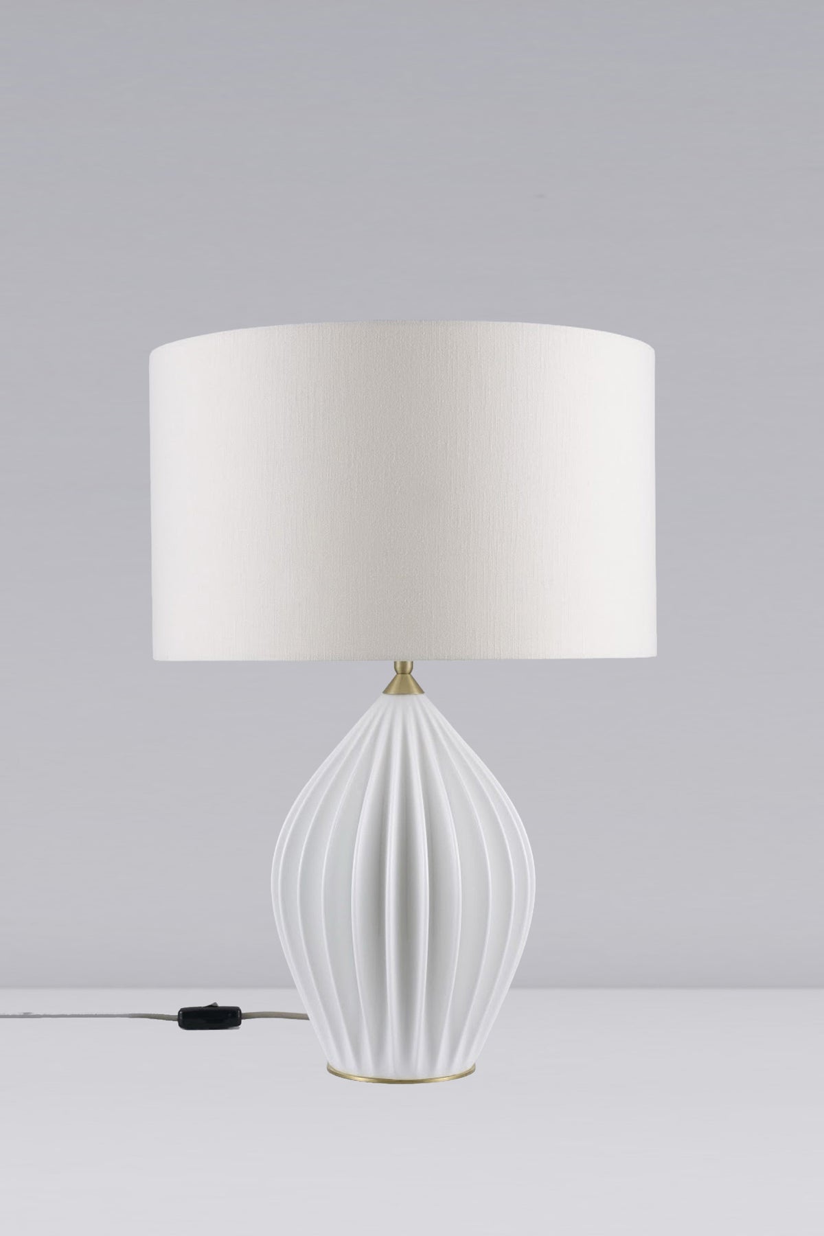 A white table lamp with a bone china base and a round lampshade, featuring a ribbed design, placed on a flat surface with a dimmer switch visible.