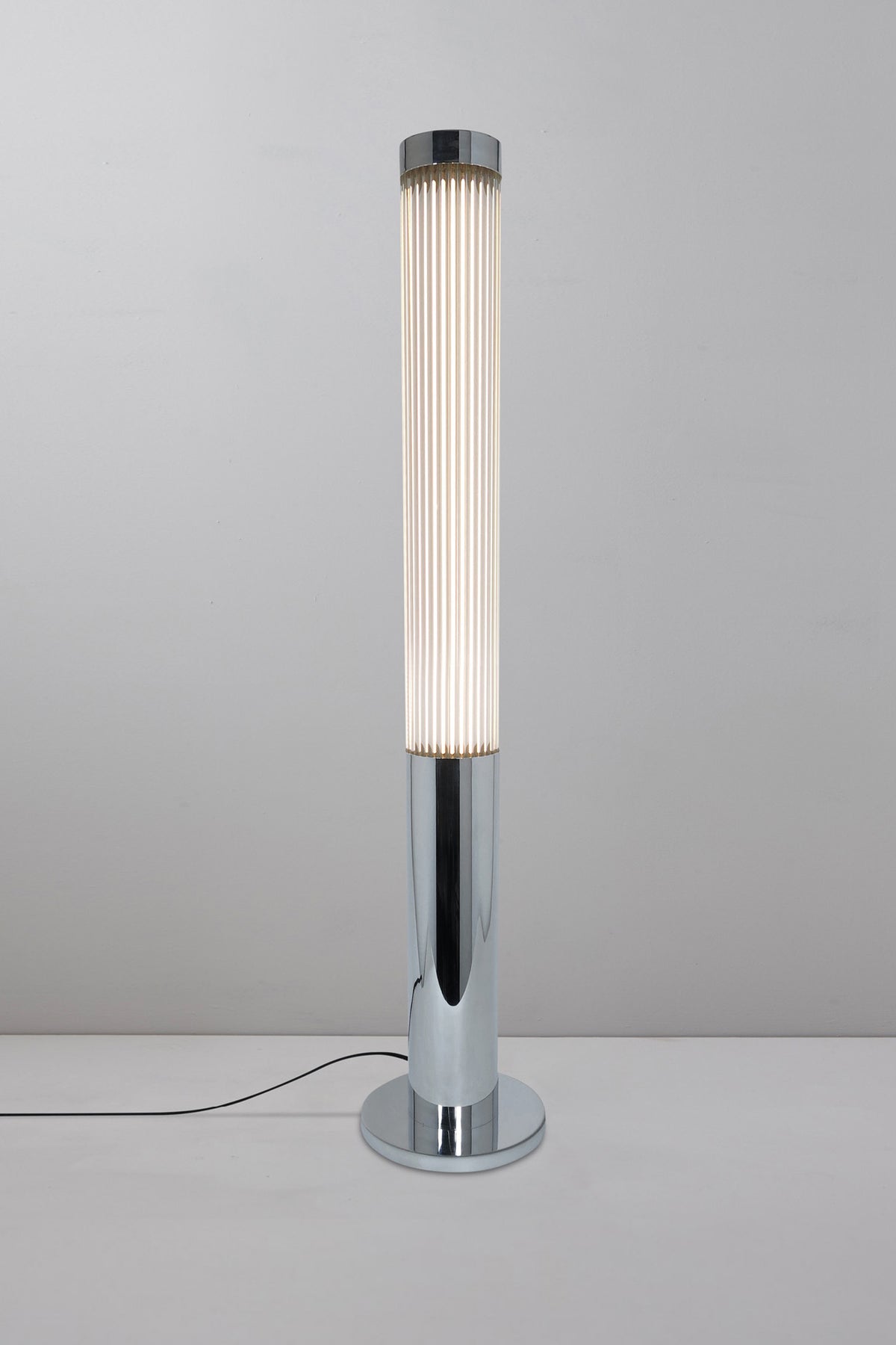 A modern silver floor lamp with a cylindrical shade, illuminated, against a white background.