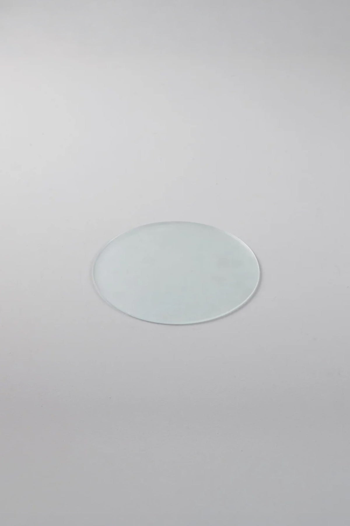 A single round, clear glass disk with a frosted, translucent finish, centered on a light gray background.